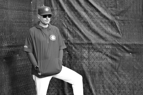 Ricky Meinhold wearing a sports team jersey and cap in front of a textured wall