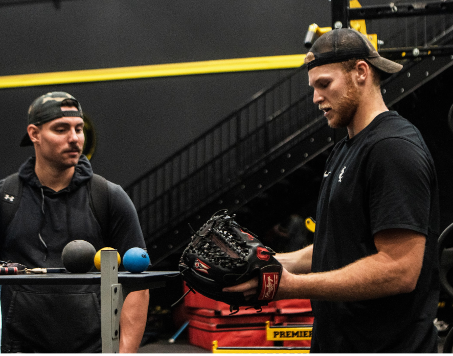 Two baseball players discuss training while examining a glove in an indoor facility at PPP